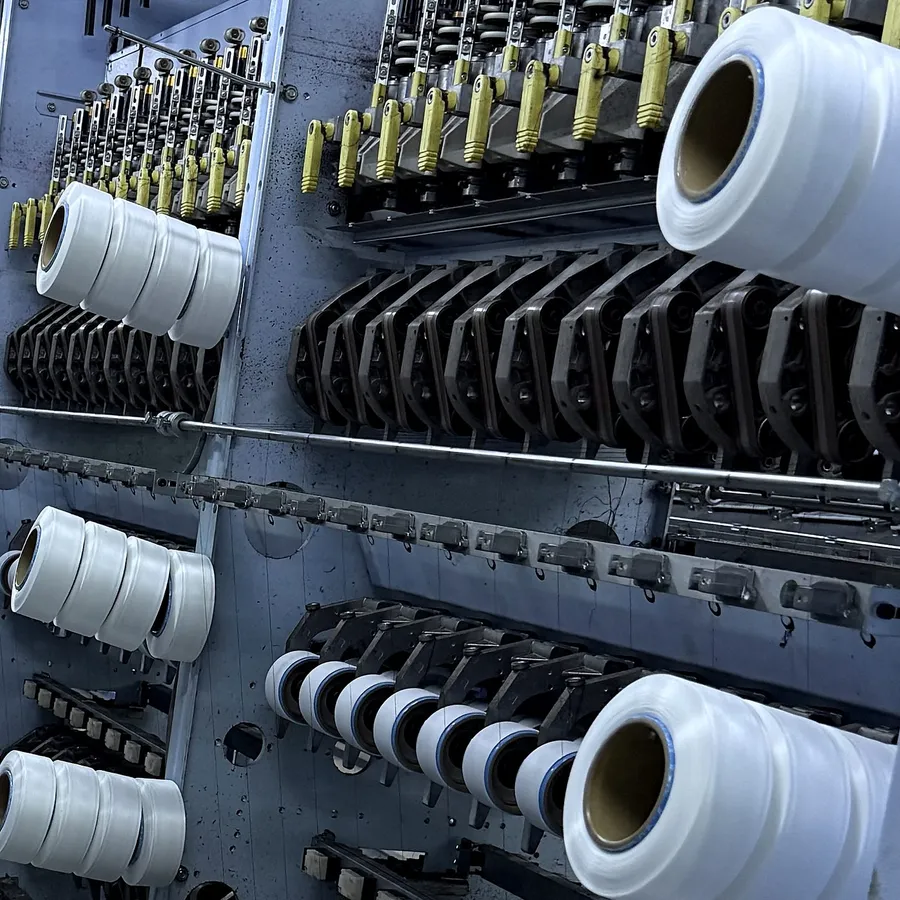 White yarn packages winding beside the yellow yarn guides of a texturing line