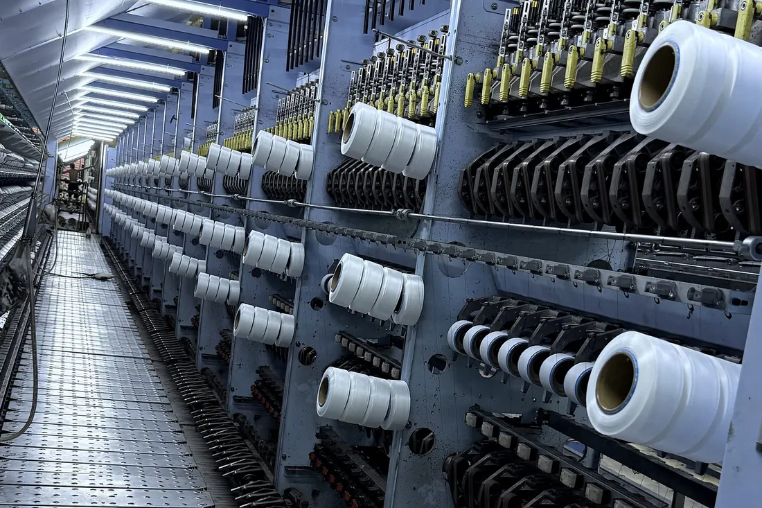 White yarn packages winding beside the yellow yarn guides of a texturing line
